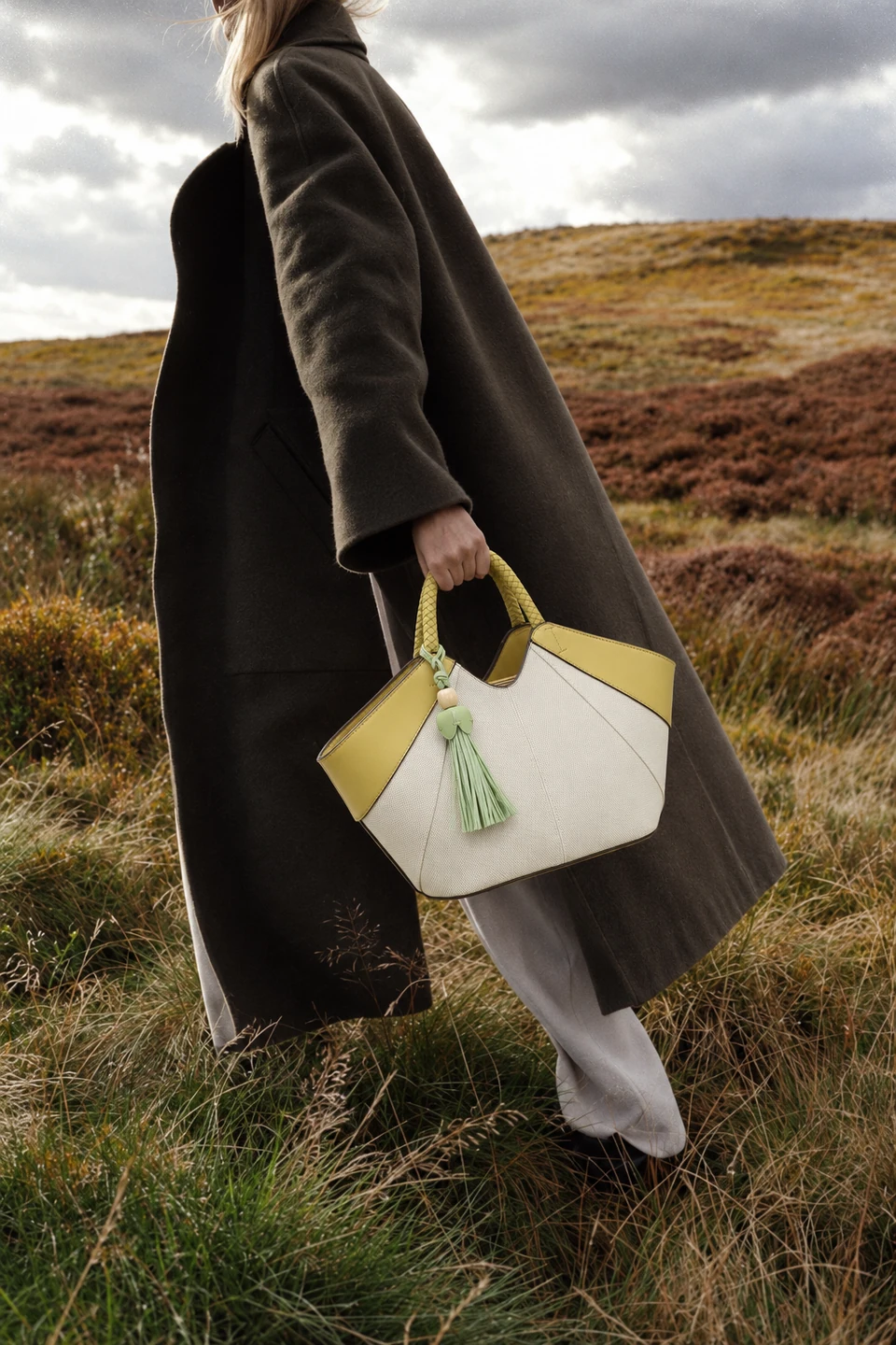 Model in a long dark olive coat walking through moorland with the cream and lemon SU QUEENA 3208 bag.