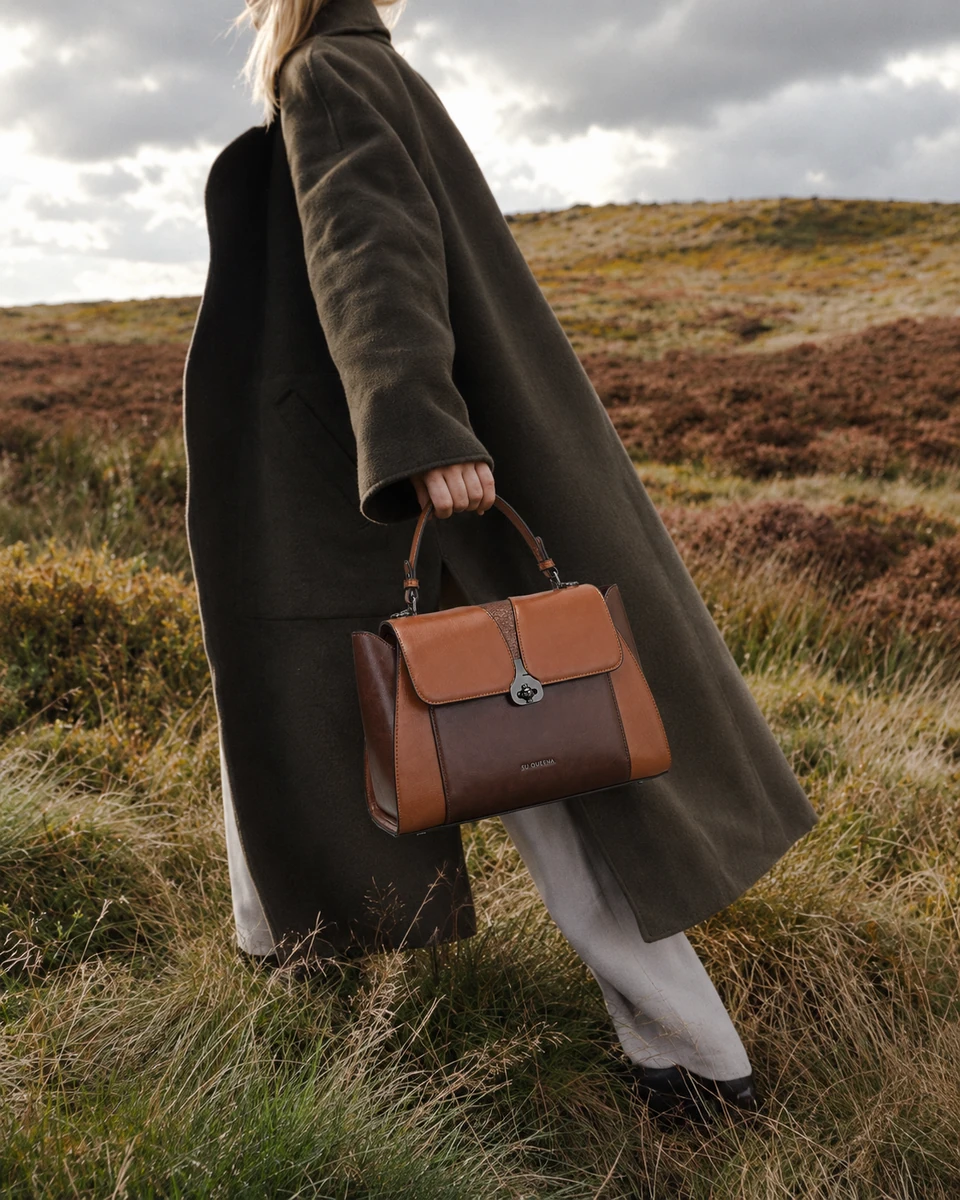 Model in a dark coat carrying the SU QUEENA 2784 brown and cognac bag through moorland.